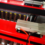 Zbliżenie na Automatyczną Formierkę Speed Former 50 SB TN HM prezentuje błyszczące metalowe cylindry, czerwono-czarną strukturę i pomarańczowo-czarne kable w czystej, nowoczesnej industrialnej konfiguracji.