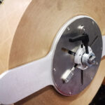 Zbliżenie dużej rolki brązowego materiału na metalowym wrzecionie z zaciskiem i śrubami, część urządzenia przemysłowego Półautomatyczna zaklejarka Easy Paper 50 SB.