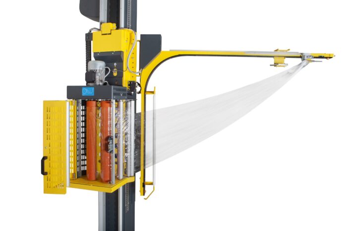Żółta półautomatyczna owijarka palet OneWrapArm owija przezroczystą folię plastikową wokół cylindrycznych przedmiotów umieszczonych w pionowej metalowej ramie z siatkowymi drzwiami.